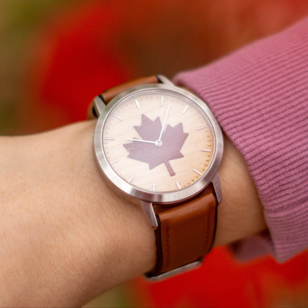 Watch with a maple leaf design on a wrist against a blurred natural background