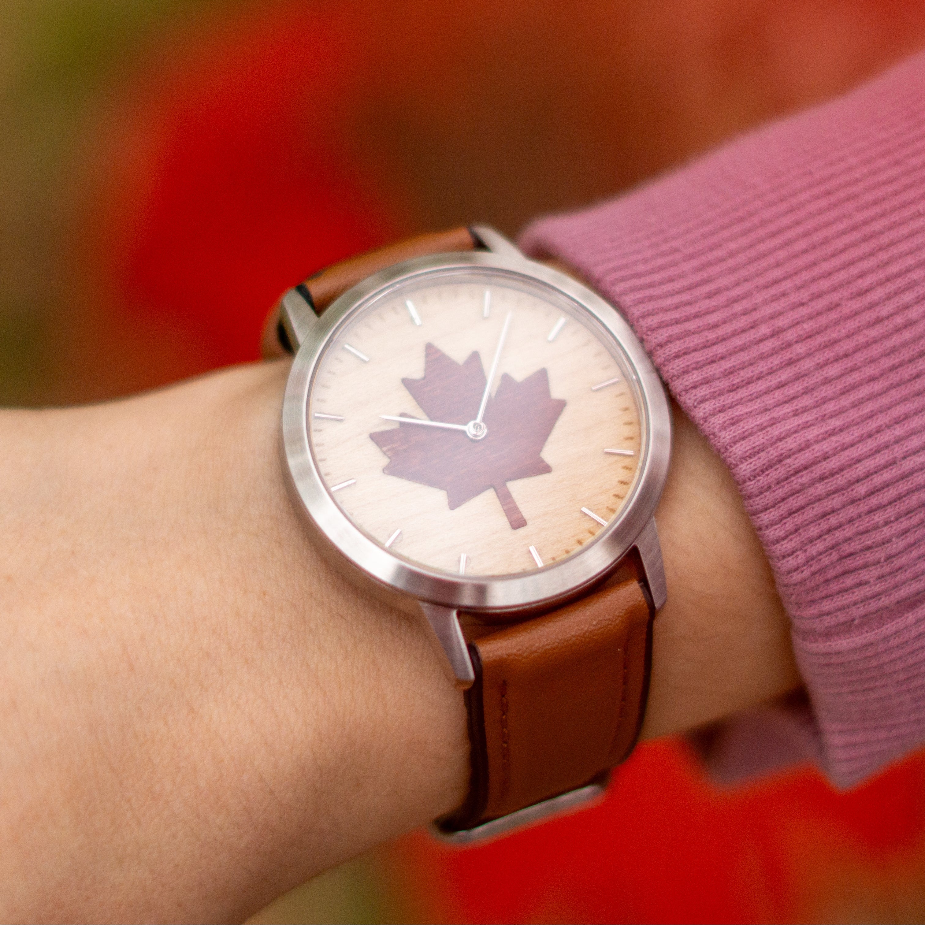 Watch with a maple leaf design on a wrist against a blurred natural background