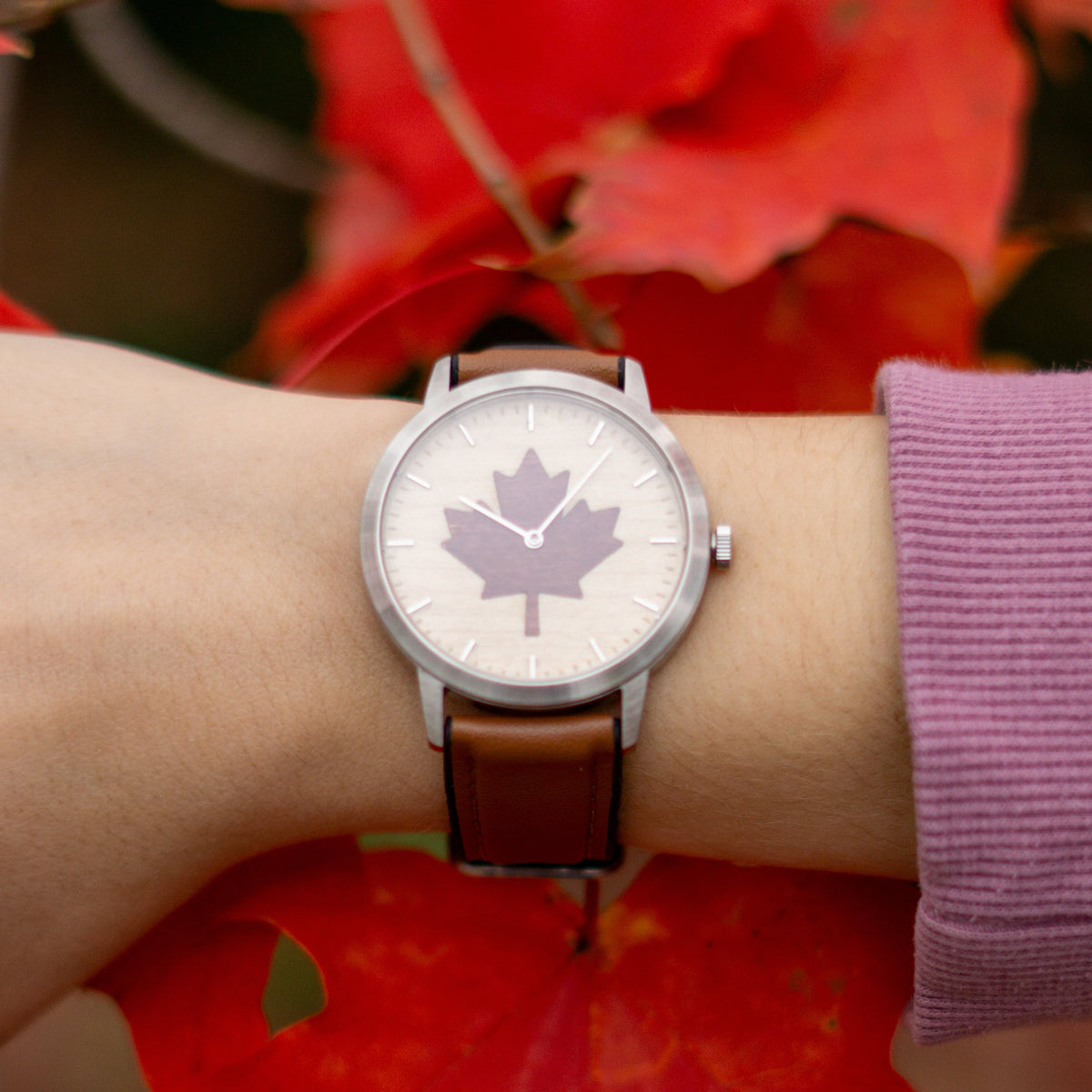 Watch with a maple leaf design on a wrist against a red leaf background